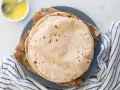 Stos świeżo upieczonych, lekko przypieczonych roti na talerzu, obok miseczki z roztopionym masłem.