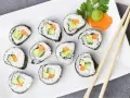 Talerz z rolkami sushi z awokado, ogórkiem i marchewką, pałeczki, wasabi i ozdobą z marchewki.
