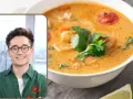 Uśmiechnięty mężczyzna w okularach obok miski aromatycznej, tradycyjnej zupy tajskiej z krewetkami i kolendrą.