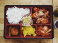 Bento box z ryżem, kurczakiem w sosie, kimchi, fasolką i żółtą rzodkiewką.