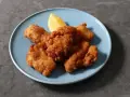 Chrupiące kawałki karaage, złociste i apetyczne, podane z ćwiartką cytryny na niebieskim talerzu.