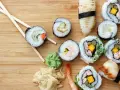 Różnorodne sushi z krewetkami, mango i warzywami, pałeczki, wasabi i marynowany imbir na drewnianym tle.