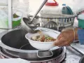 Gorący bulion wlewany jest do miski z wietnamskim jedzeniem: makaronem, klopsikami i mięsem.