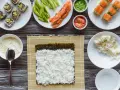 Przygotowanie sushi: ryż, nori, łosoś, awokado, wasabi i marynowany imbir na drewnianym blacie.