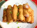 Chrupiące paluszki surimi w cieście, posypane szczypiorkiem, prezentują się apetycznie na białym talerzu.