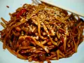 Makaron chow mein z sezamem i papryką na białym talerzu, z pałeczkami.