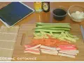Pokrojone składniki do sushi: ogórek, łosoś, paluszki krabowe, awokado, sezam, sos sojowy, ryż i nori.