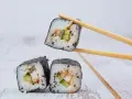 Trzy kawałki sushi z ryżem, ogórkiem i rybą, jeden podniesiony pałeczkami. Idealne do sosu sojowego, czyli zalewa do sushi.