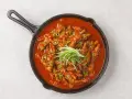 Kurczak w sosie gochujang, posypany sezamem i zieloną cebulką, podany w żeliwnej patelni.
