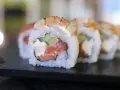 Pyszne uramaki z łososiem, awokado i serkiem śmietankowym, posypane krewetkami.