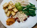 Talerz z pokrojonym tofu, orzeszkami ziemnymi, szczypiorkiem, kiełkami fasoli mung, limonkami i płatkami chili.