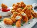 Chrupiące kawałki kurczaka w panierce z bułki tartej panko, podane z ketchupem i posypane natką pietruszki.
