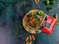 Aksamitny kurczak po kantońsku z brokułami i marchewką, gotowy do podania. Obok paczka pasty do stir-fry.