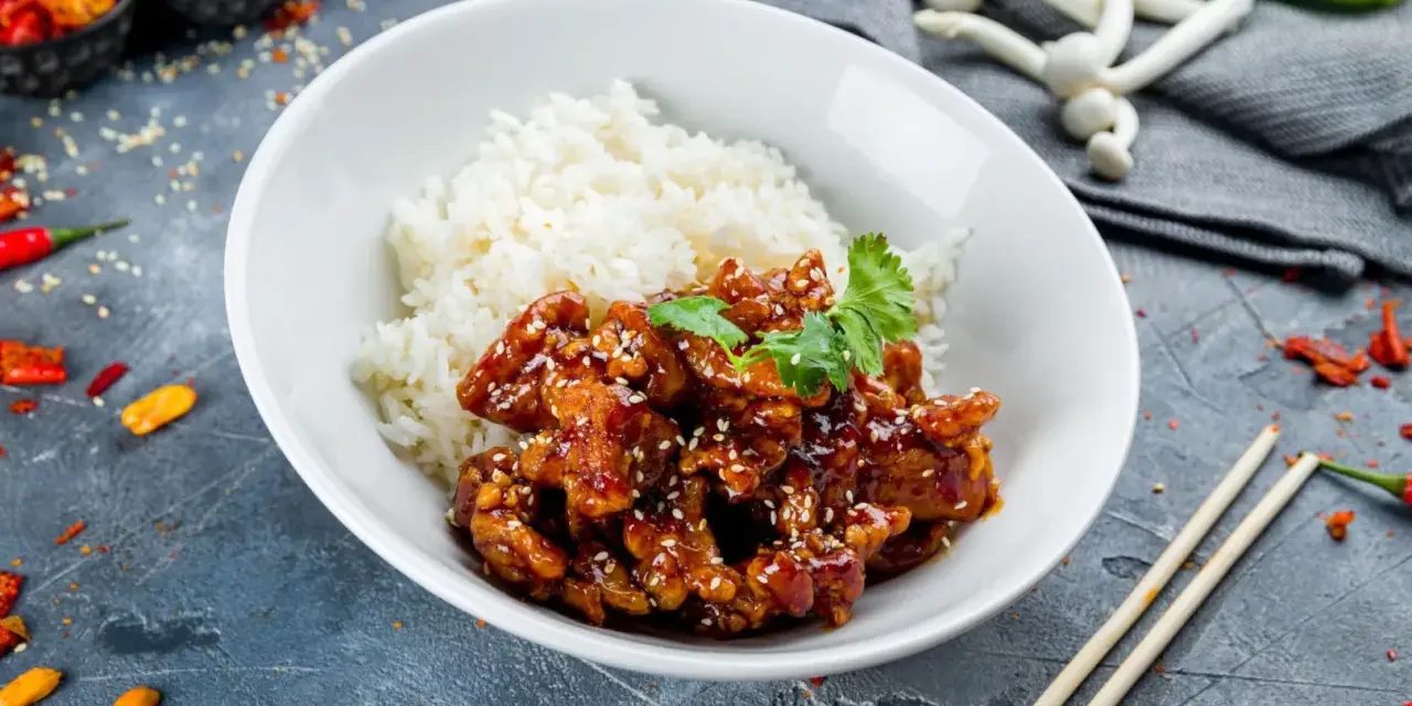 Pyszny kurczak bac bo w sosie z sezamem, podany z ryżem. Obok pałeczki i papryczki chili.