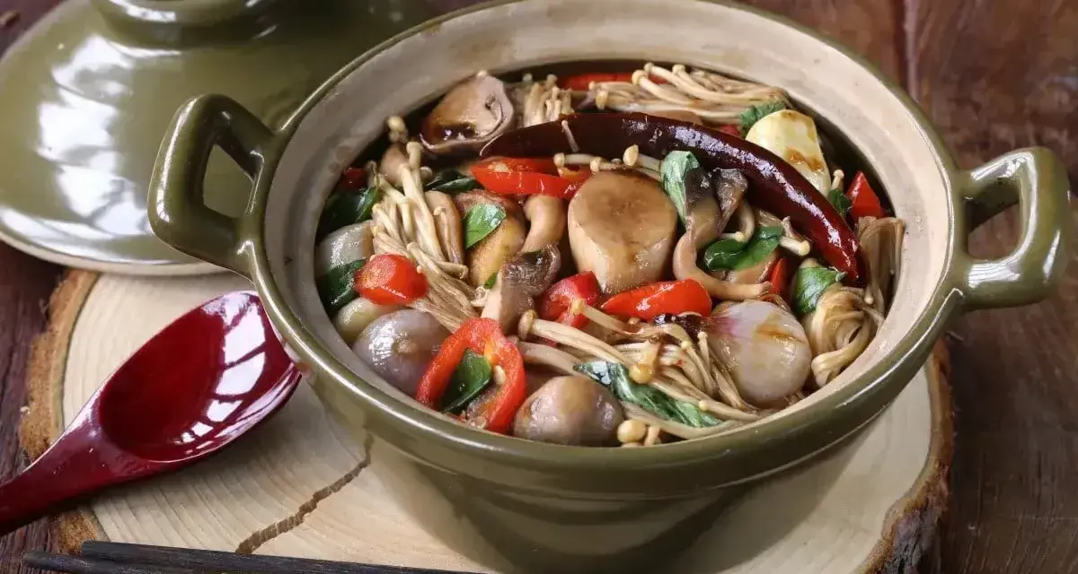 Gęsta zupa z grzybkami mun, papryczkami chili i innymi warzywami w glinianym garnku.