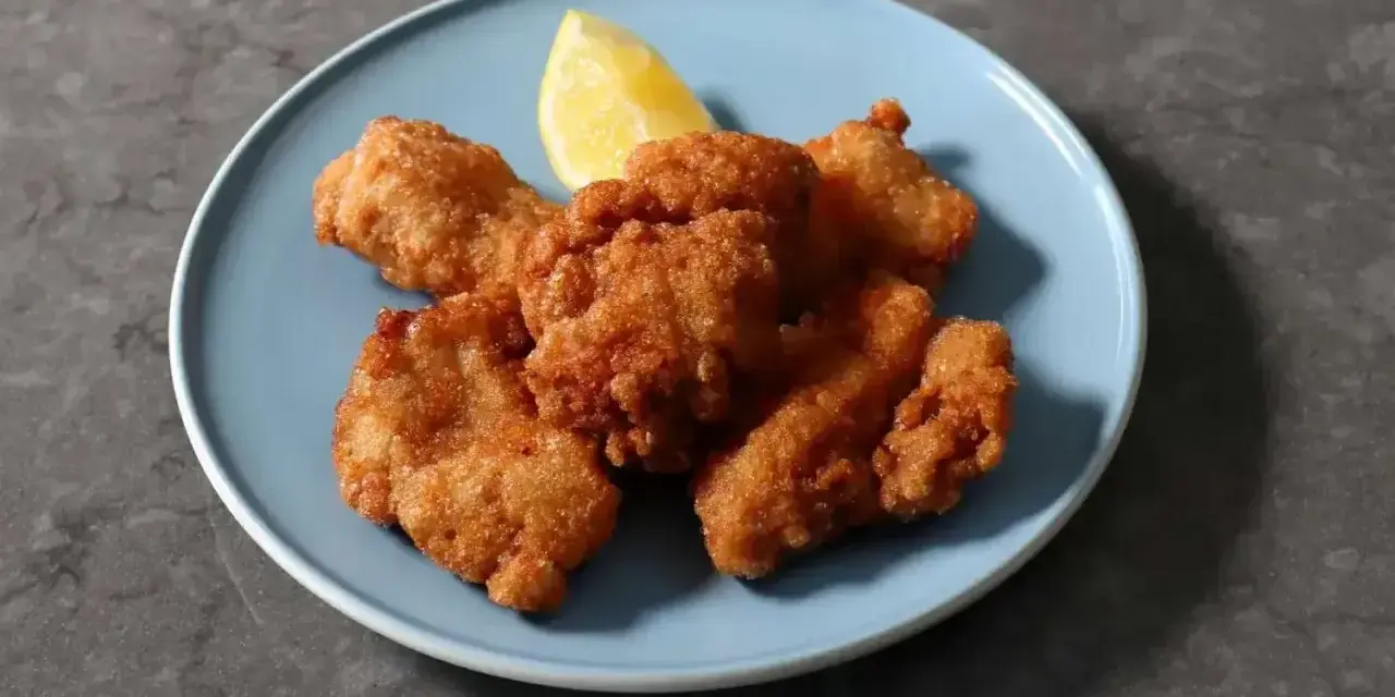 Chrupiące kawałki karaage, złociste i apetyczne, podane z ćwiartką cytryny na niebieskim talerzu.