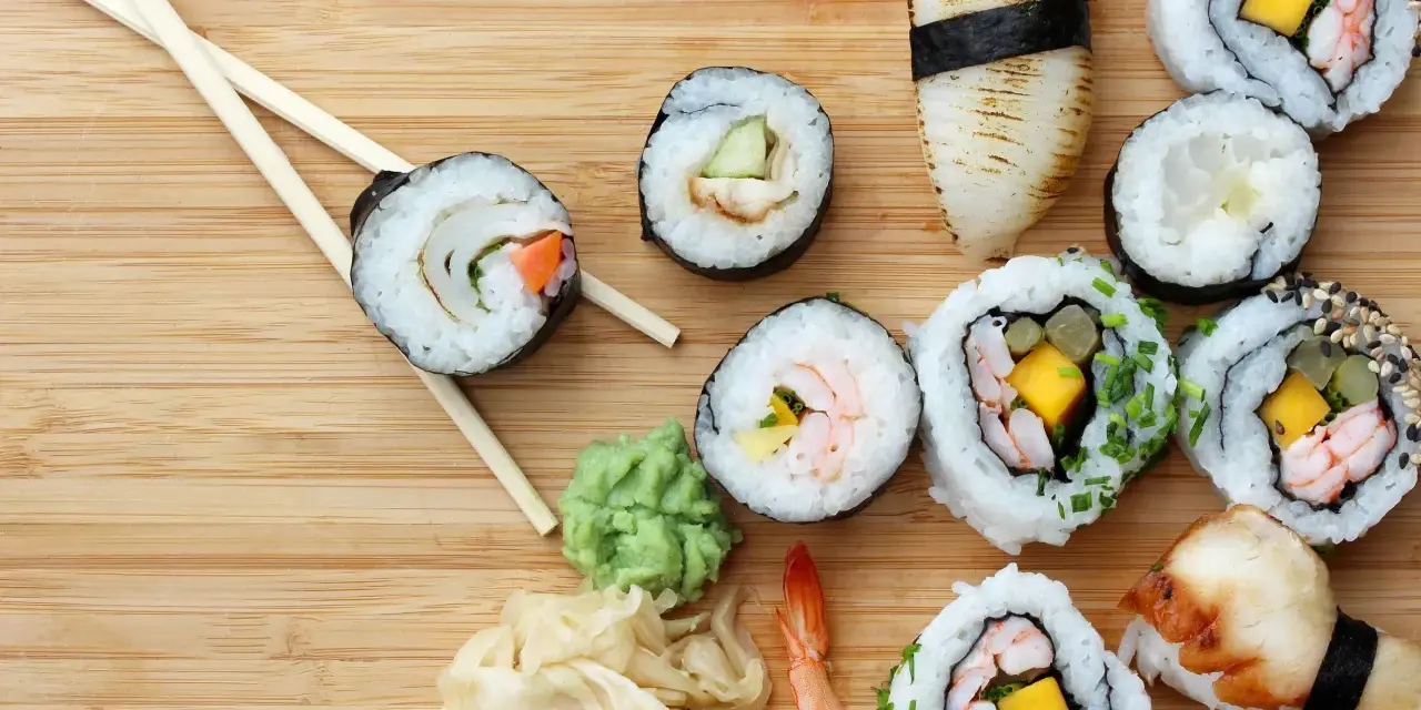 Różnorodne sushi z krewetkami, mango i warzywami, pałeczki, wasabi i marynowany imbir na drewnianym tle.