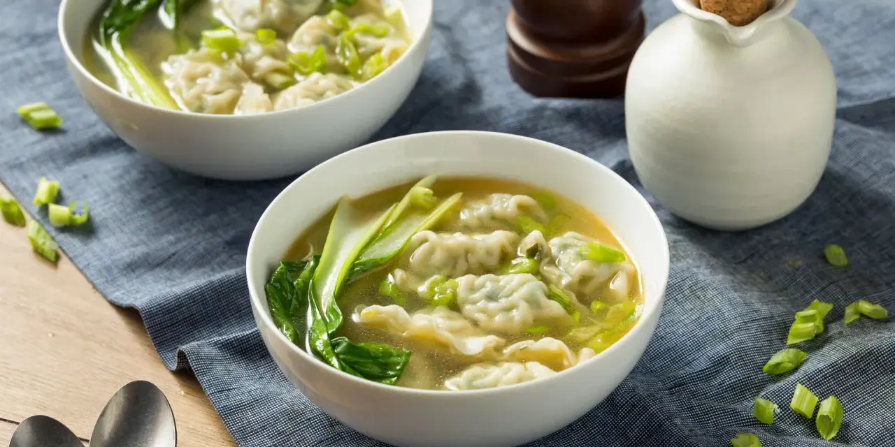 Dwie miseczki aromatycznej zupy won ton z zielonymi warzywami i posiekanym szczypiorkiem.