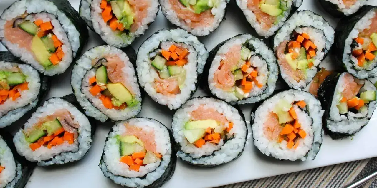 Ułożone na talerzu rolki sushi z łososiem, awokado, ogórkiem i marchewką. Widać, co do sushi do środka, czyli świeże składniki.