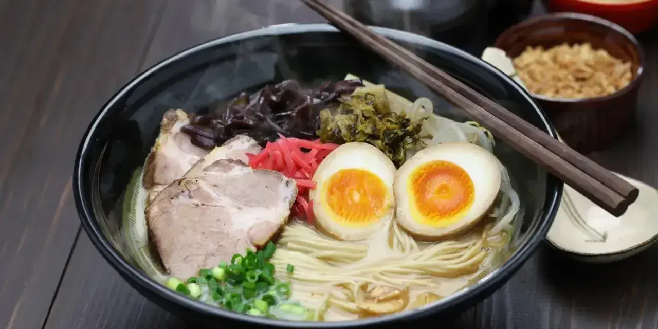 Parujący ramen: makaron, plastry wieprzowiny, jajko na pół, szczypiorek i grzyby. Pyszne danie, które rozgrzewa.