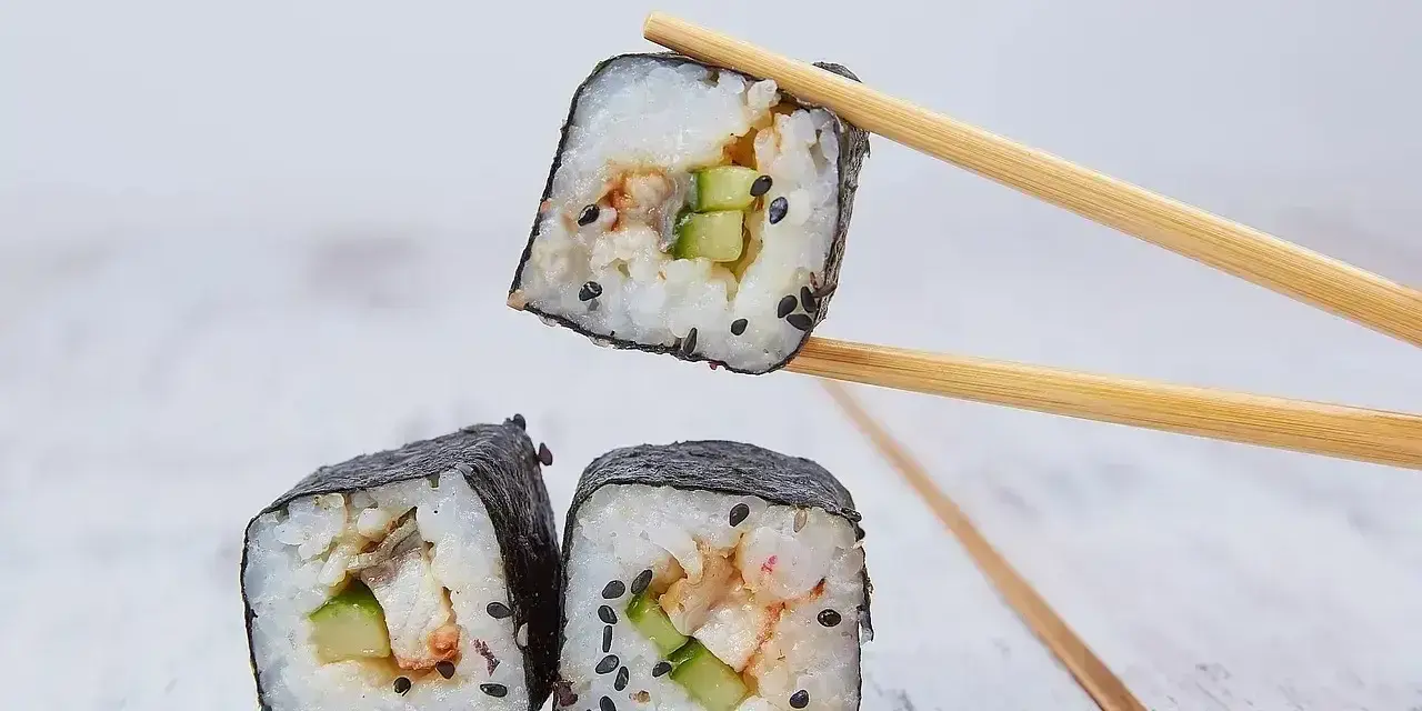 Trzy kawałki sushi z ryżem, ogórkiem i rybą, jeden podniesiony pałeczkami. Idealne do sosu sojowego, czyli zalewa do sushi.