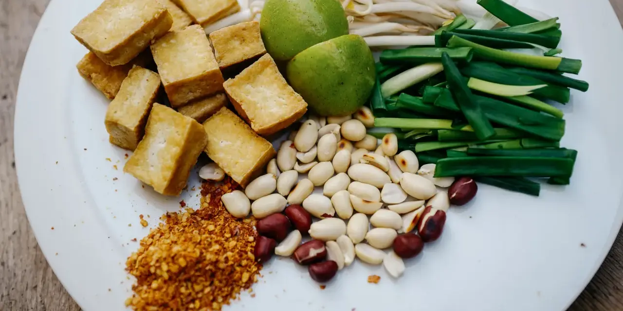 Talerz z pokrojonym tofu, orzeszkami ziemnymi, szczypiorkiem, kiełkami fasoli mung, limonkami i płatkami chili.