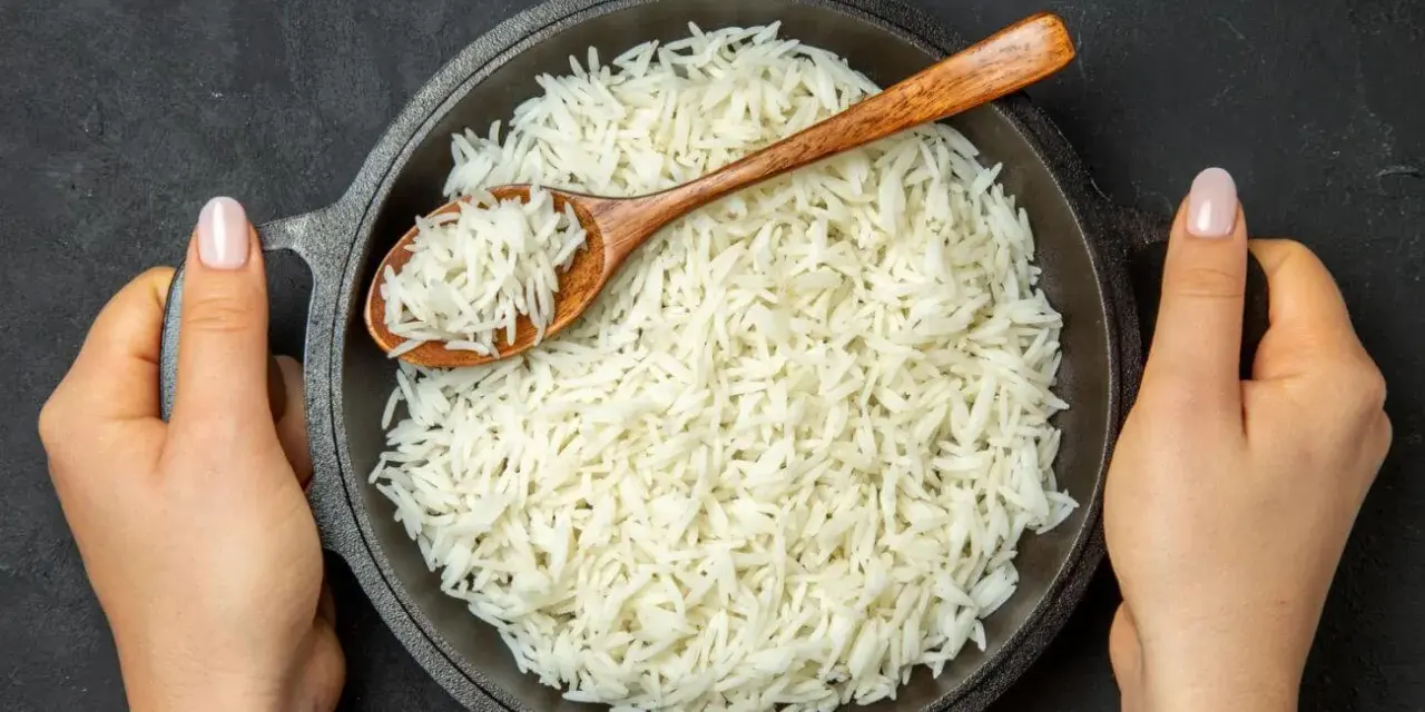 Sypki ryż basmati w misce, nabierany drewnianą łyżką, trzymany przez dwie dłonie.
