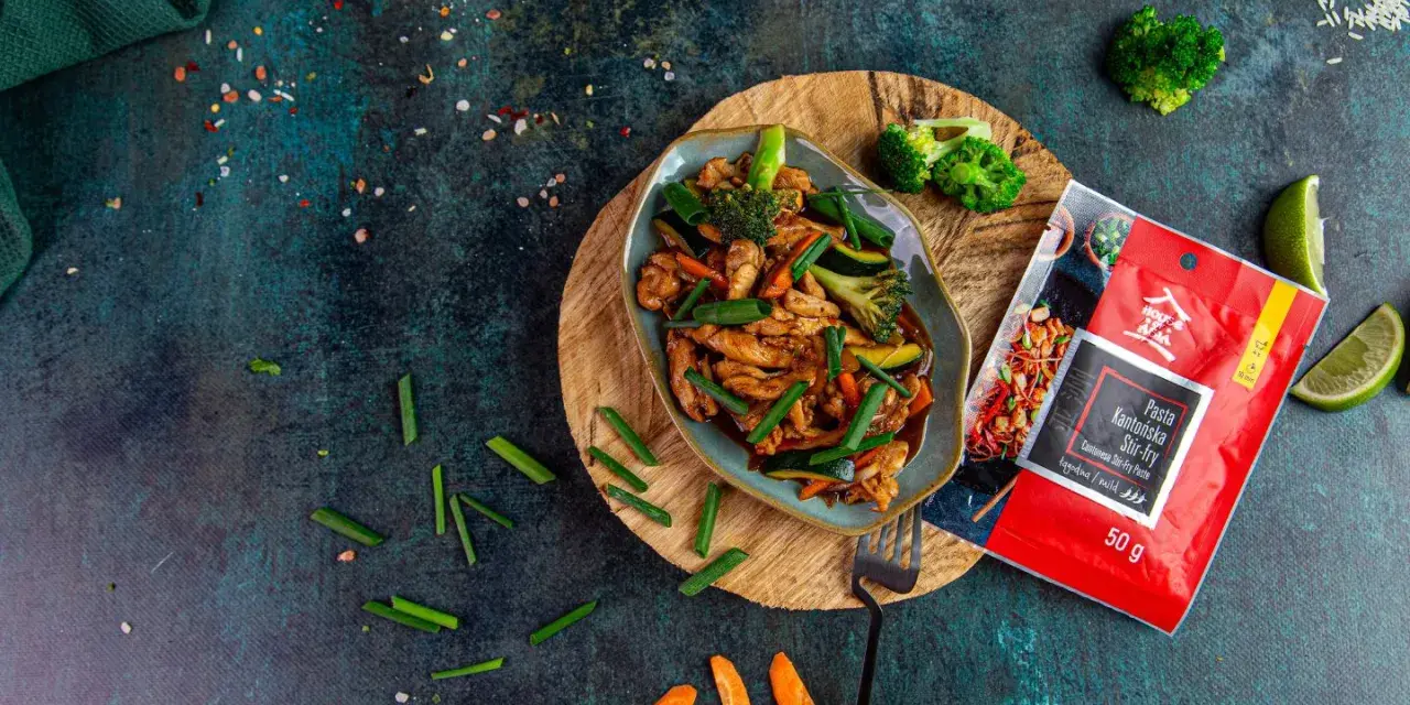 Aksamitny kurczak po kantońsku z brokułami i marchewką, gotowy do podania. Obok paczka pasty do stir-fry.