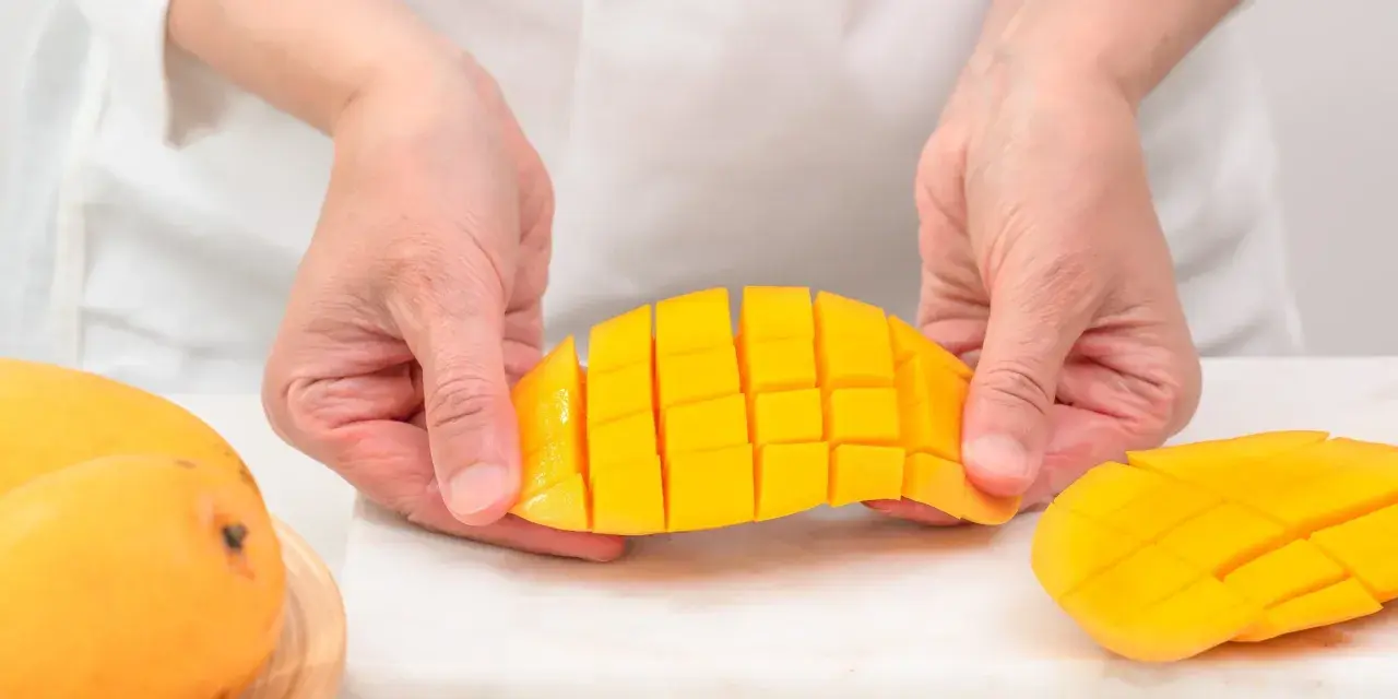 Ręce trzymają pokrojonego w kostkę mango. Ten soczysty owoc jest gotowy do jedzenia.