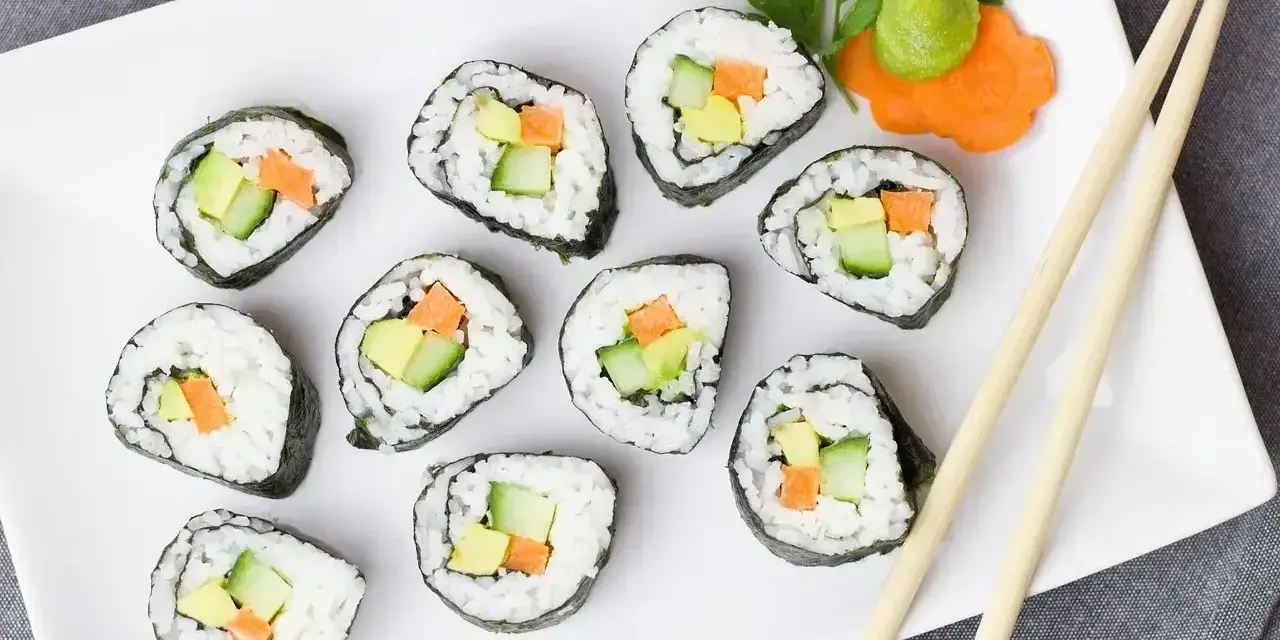 Smaczne futomaki z awokado, ogórkiem i marchewką, udekorowane natką pietruszki i wasabi.