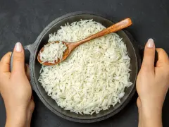 Sypki ryż basmati w misce, nabierany drewnianą łyżką, trzymany przez dwie dłonie.