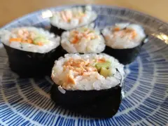 Pięć kawałków sushi z łososiem, ryżem i warzywami na niebiesko-białym talerzu.