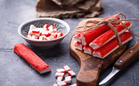 Surimi co to? Paluszki krabowe, pokrojone i całe, na desce i w miseczce, gotowe do sałatki.