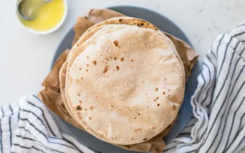 Stos świeżo upieczonych, lekko przypieczonych roti na talerzu, obok miseczki z roztopionym masłem.