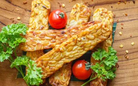 Złociste kawałki tempeh, smażone na złoto, z pomidorkami i natką pietruszki. Tempeh co to? To pyszna, roślinna alternatywa.