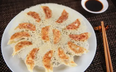 Chrupiące pierożki gyoza ułożone na talerzu, z chrupiącą, złotą panierką. Obok miseczka sosu sojowego i pałeczki.