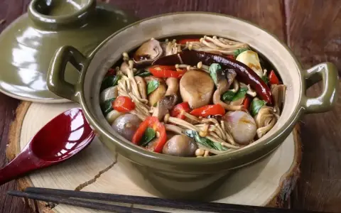 Gęsta zupa z grzybkami mun, papryczkami chili i innymi warzywami w glinianym garnku.