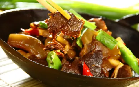 Chopsticks podnoszą kawałek aromatycznej wołowiny po chińsku z miski pełnej pysznego dania z warzywami.