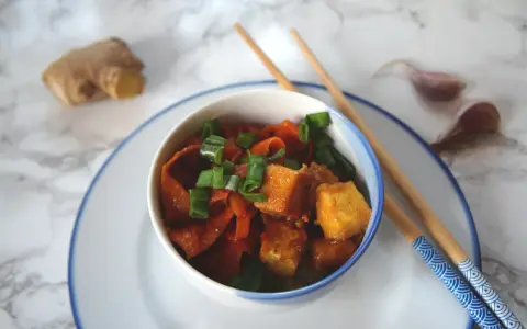 Pyszne dania z tofu z marchewką i szczypiorkiem, gotowe do jedzenia pałeczkami. Obok imbir i czosnek.