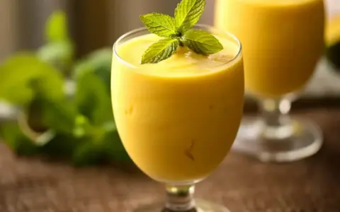 Orzeźwiający mango lassi, gęsty i kremowy, ozdobiony listkiem mięty. Idealny na upalny dzień.