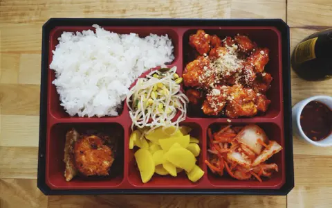 Bento box z ryżem, kurczakiem w sosie, kimchi, fasolką i żółtą rzodkiewką.
