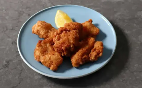 Chrupiące kawałki karaage, złociste i apetyczne, podane z ćwiartką cytryny na niebieskim talerzu.
