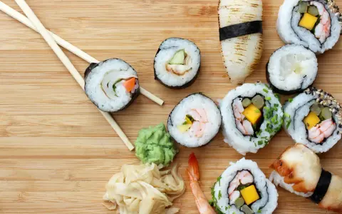 Różnorodne sushi z krewetkami, mango i warzywami, pałeczki, wasabi i marynowany imbir na drewnianym tle.