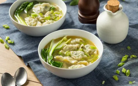 Dwie miseczki aromatycznej zupy won ton z zielonymi warzywami i posiekanym szczypiorkiem.