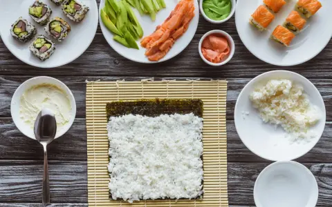 Przygotowanie sushi: ryż, nori, łosoś, awokado, wasabi i marynowany imbir na drewnianym blacie.