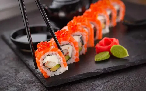 Chopsticks podnoszą kawałek sushi z łososiem i ikrą. Czy sushi jest lekkostrawne? Zależy od składników, ale to wygląda apetycznie.
