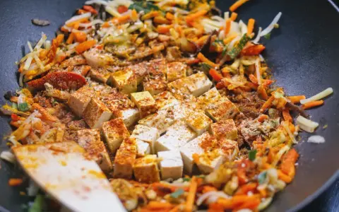Kawałki tofu i kolorowe warzywa po chińsku smażą się na patelni wok, przyprawione kurkumą i papryką.