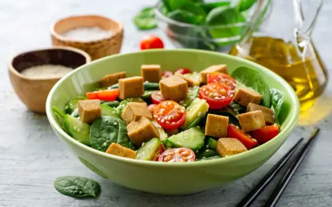 Pyszna sałatka z chrupiącym, pieczonym tofu, świeżymi pomidorkami, ogórkiem i szpinakiem. Idealna na lekki posiłek.