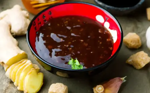Miseczka z aromatycznym sosem teriyaki, obok świeży imbir, czosnek i brązowy cukier.