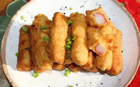 Chrupiące paluszki surimi w cieście, posypane szczypiorkiem, prezentują się apetycznie na białym talerzu.